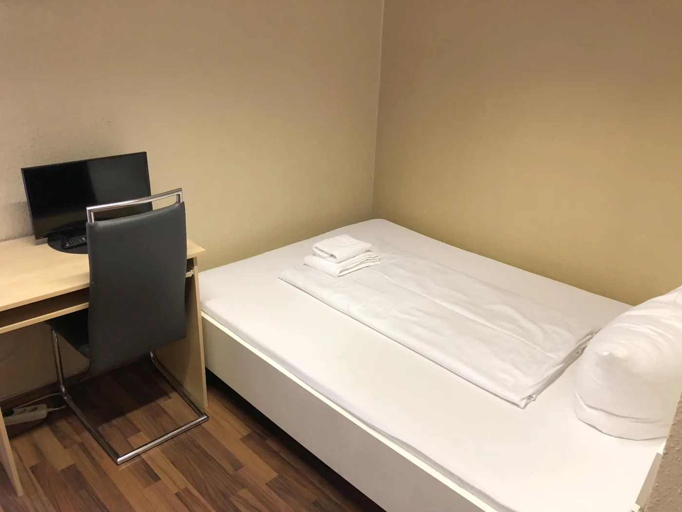 Einzelzimmer mit Schreibtisch, Stuhl und Fernseher